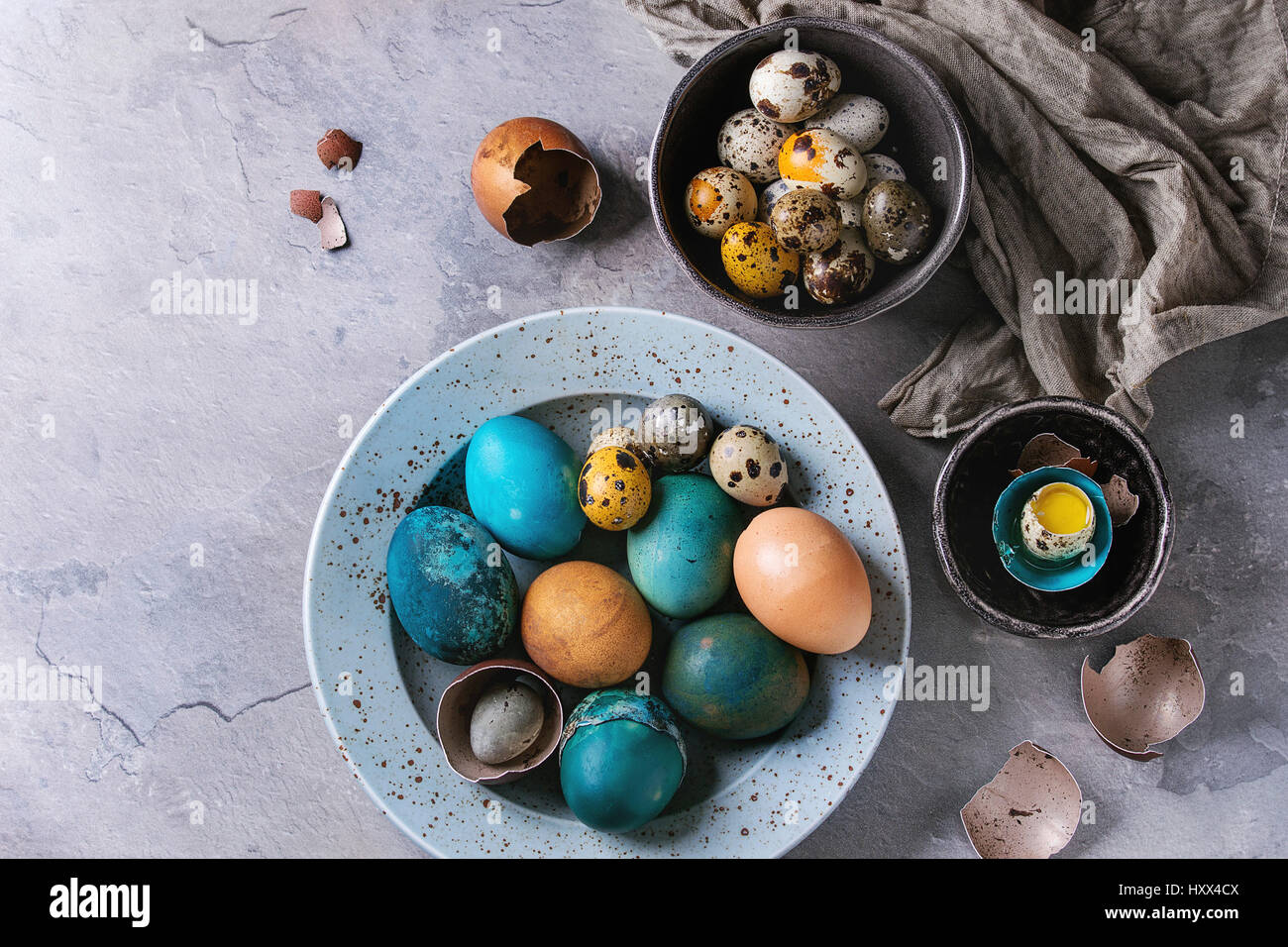 Farbige Ostern blau braun Hühner- und Wachteleier, ganzen und gebrochenen mit Eigelb in der Schale in gefleckte Platte und schwarzen Schalen mit Textil über grau strukturiert Stockfoto