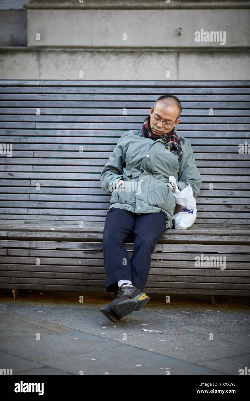 Asiatischer Mann schlafen auf einer öffentlichen Sitzbank in der Nähe von Petersplatz, Manchester City Centre, England, UK. Stockfoto