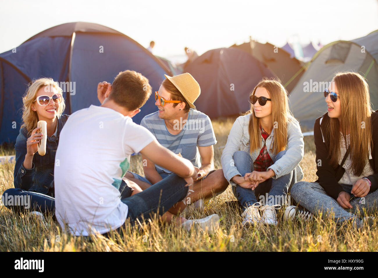Gruppe von Teenager-Jungen und Mädchen im Sommer-Musikfestival, sitzen auf dem Boden vor Zelten ausruhen und Essen Stockfoto