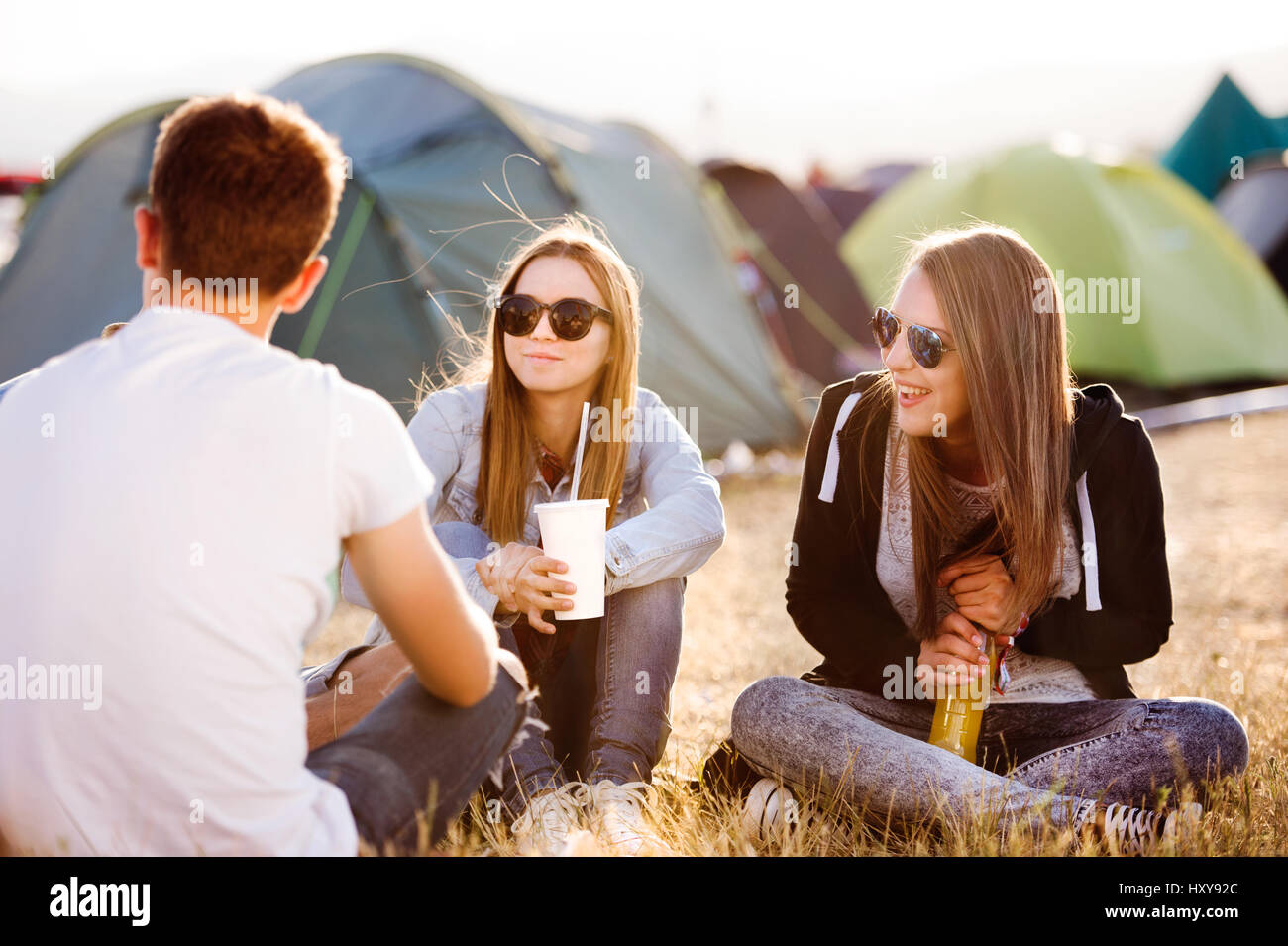 Gruppe von Teenager-Jungen und Mädchen im Sommer-Musikfestival, sitzen auf dem Boden vor Zelten, Essen und trinken Stockfoto