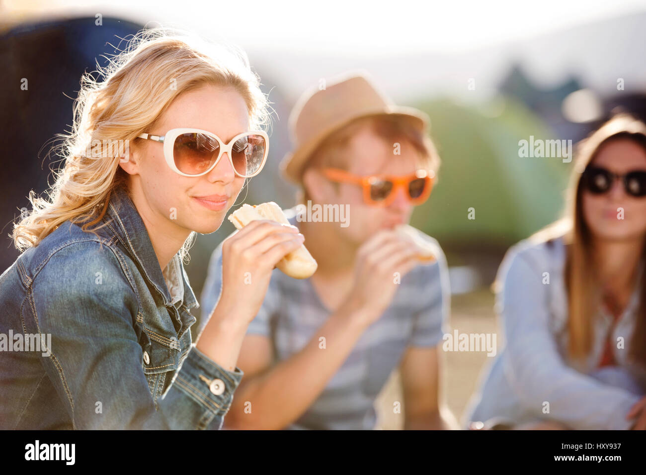 Gruppe von Teenager-Jungen und Mädchen im Sommer-Musikfestival, sitzen auf dem Boden vor Zelten Essen Stockfoto
