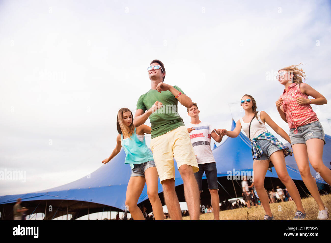 Gruppe von Teenager-Jungen und Mädchen im Sommer-Musikfestival, tanzen vor grossen Zelt, sonnigen Tag Stockfoto