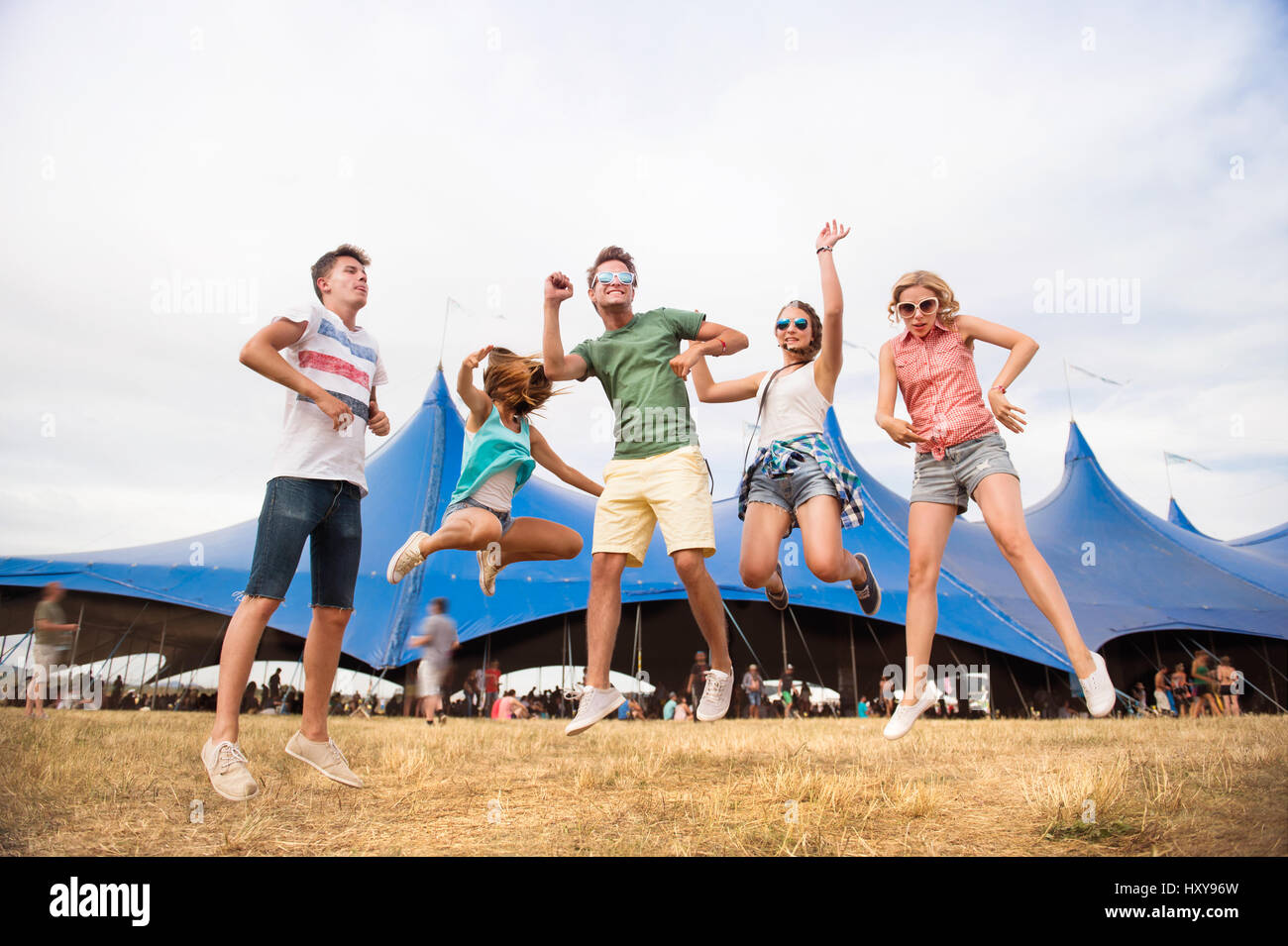 Gruppe von Teenager-Jungen und Mädchen im Sommer-Musikfestival, tanzen und springen vor grossen Zelt, sonnigen Tag Stockfoto