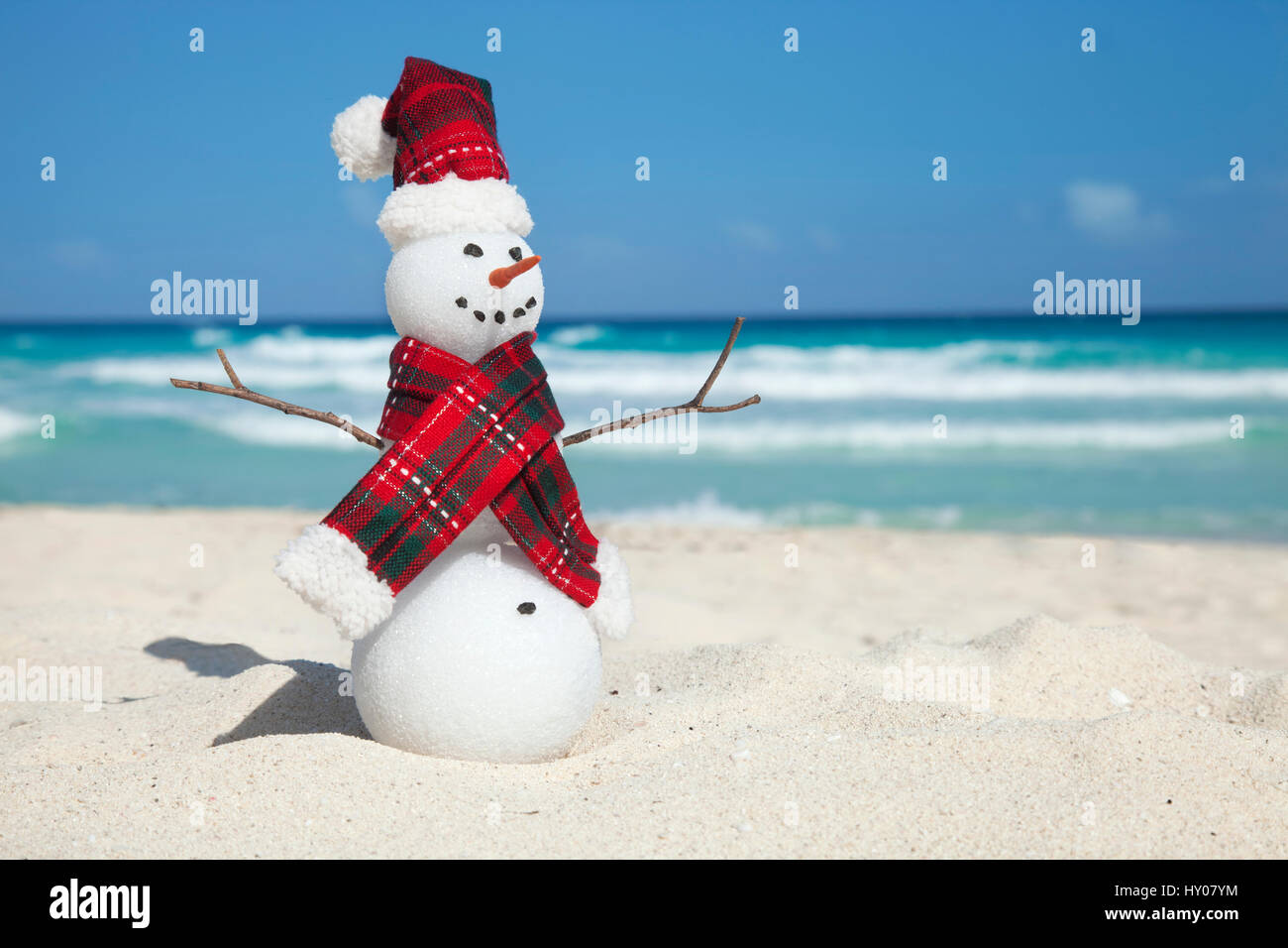 Miniatur-Schneemann mit Hut und Schal am Strand mit der blauen karibischen hinter Stockfoto