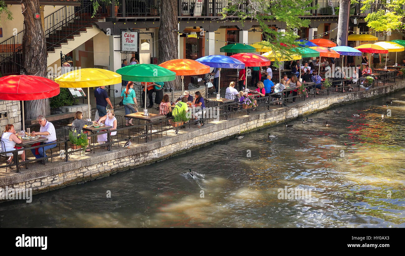 Touristen beim Mittagessen unter bunten Sonnenschirmen entlang des San Antonio River Walk in San Antonio, Texas Stockfoto