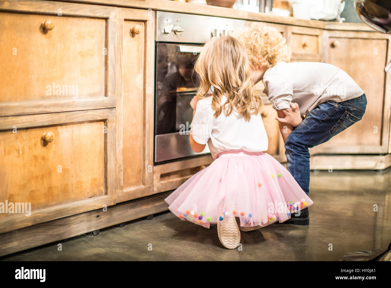 Kleine Jungen und Mädchen auf der Suche im Ofen in der Küche Stockfoto