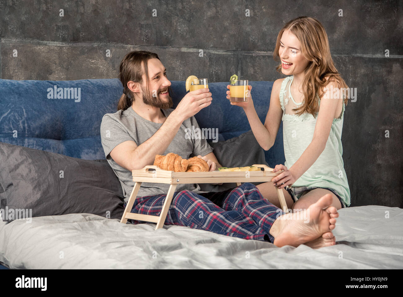 Junge glückliche Paar frühstückt im Bett und trinkt Orangensaft Stockfoto