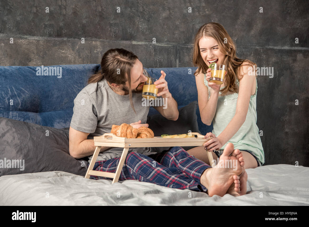 Junge glückliche Paar frühstückt im Bett und trinkt Orangensaft Stockfoto