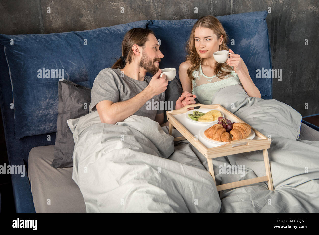 Junge glückliche Paar frühstückt im Bett und trinkt Kaffee Stockfoto