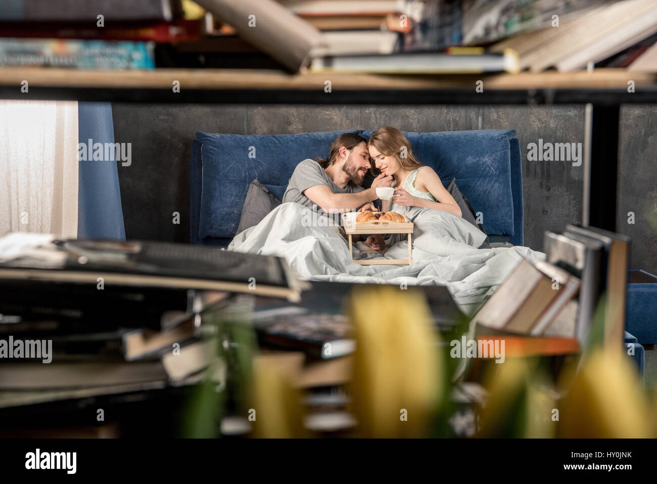 Blick durch das Bücherregal des jungen Paares hat das Frühstück im Bett Stockfoto