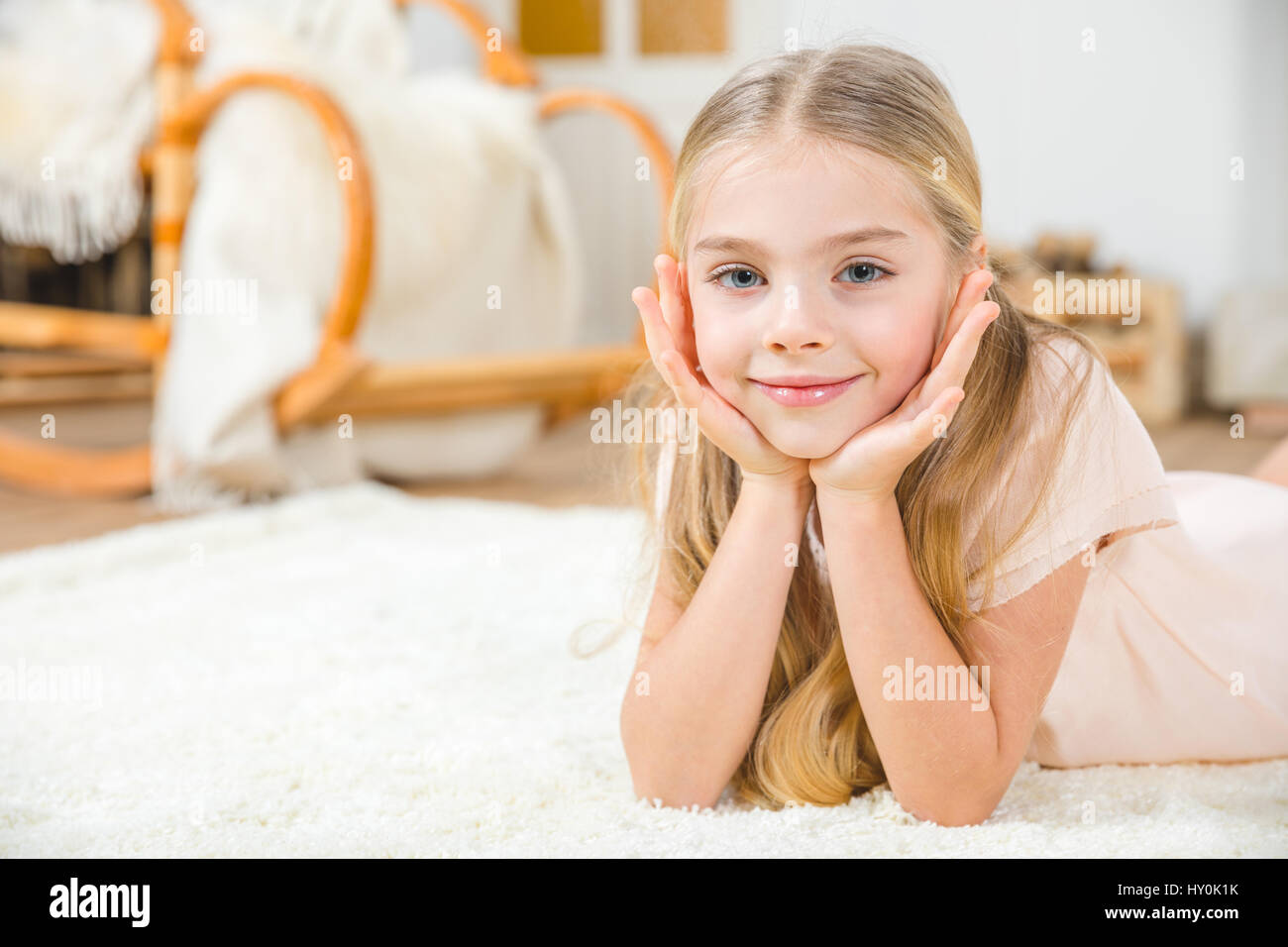 Niedliche kleine Mädchen auf weißen Teppich liegend und lächelt in die Kamera Stockfoto