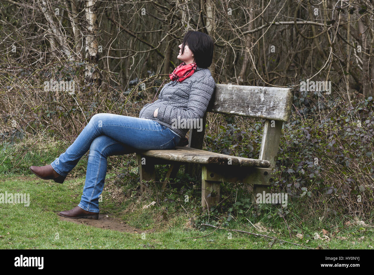 Junge Erwachsene denken Frau ruht auf Holzbank im Park. Kalten Herbstwetter. Horizontale Ernte Stockfoto