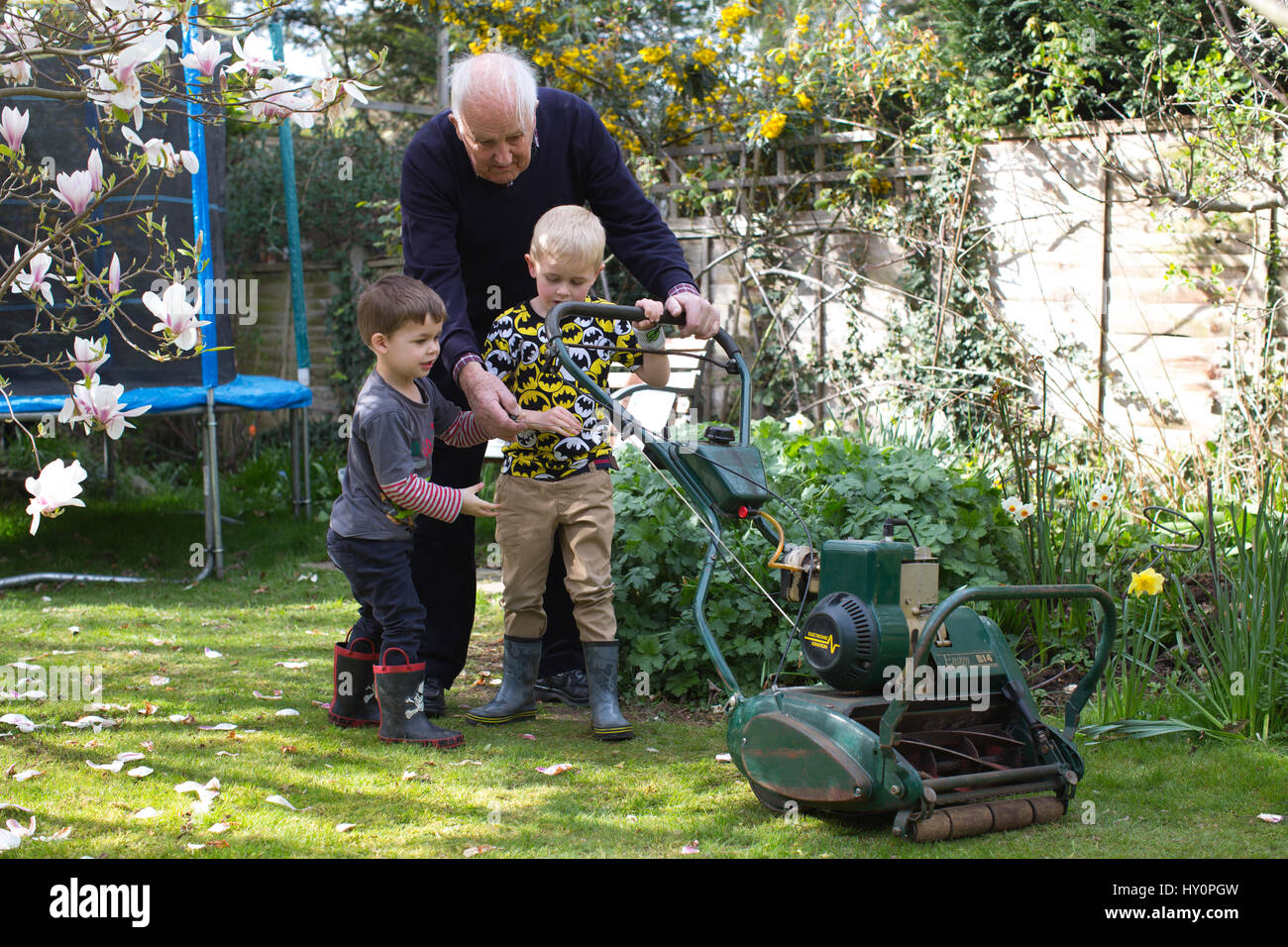 Rentner, die versuchen, starten Sie einen Benzin-Rasenmäher in einem englischen Wohn Garten auf einer Feder Nachmittag, Surrey, England, Vereinigtes Königreich Stockfoto