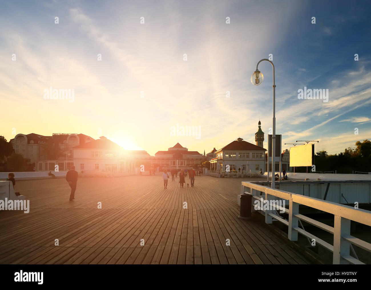 Breite Promenade bei Sonnenuntergang. Strahlende Sonne beleuchten Holzsteg am Abend. Paare, die zu Fuß am Boardwalk in Abend. Glänzend unterwegs Hintergrund. Stockfoto