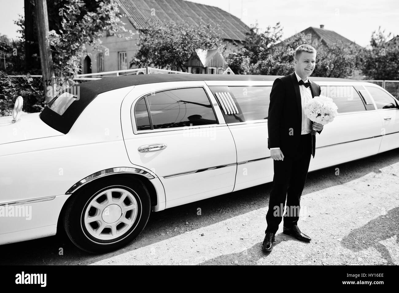 Stilvolle Bräutigam mit Brautstrauß auf Hände in der Nähe von Limousinen. Stockfoto