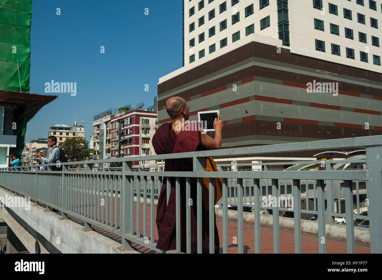 27.01.2017, Yangon, Republik der Union Myanmar, Asien - ein buddhistischer Mönch steht auf einer Fußgängerbrücke und nimmt Bilder der neuen sule Square. Stockfoto