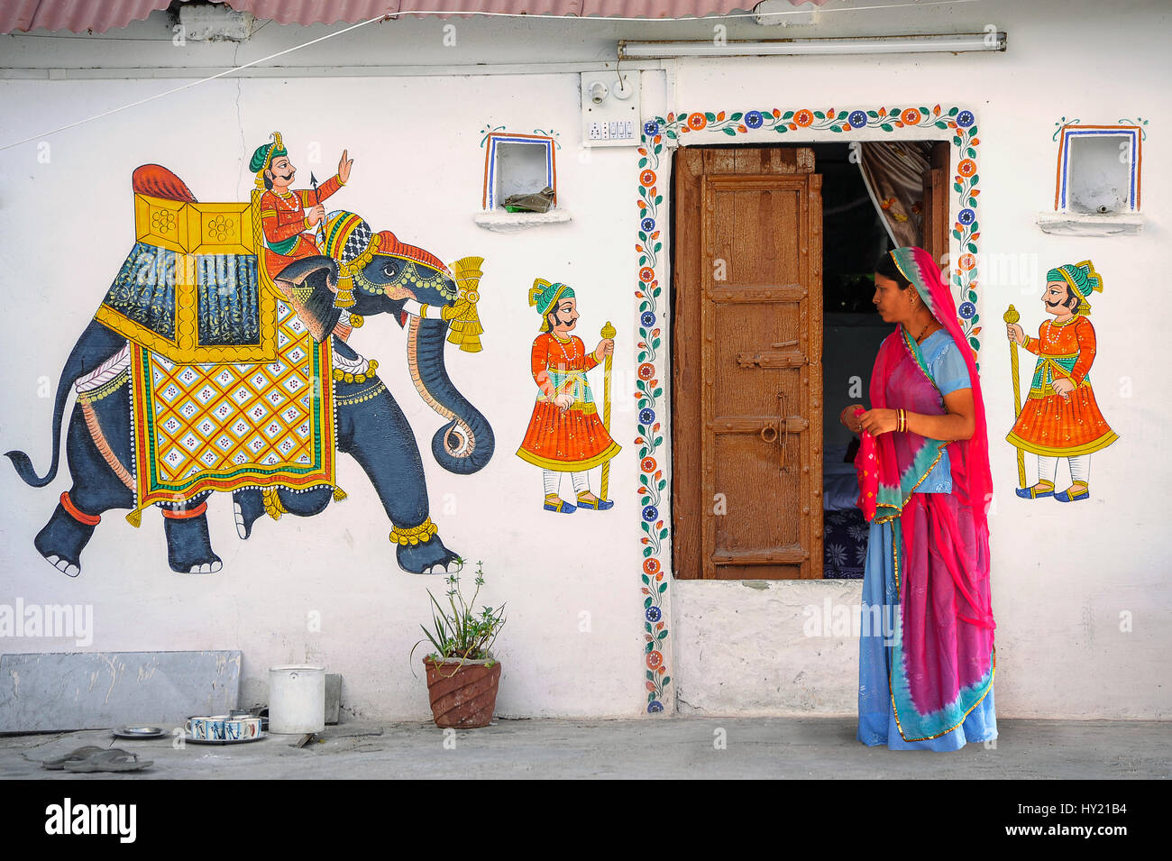 Eine Frau in einem lebendigen Sari steht vor einem Haus Udaipur mit Rajput Wandbilder gemalt. Stockfoto