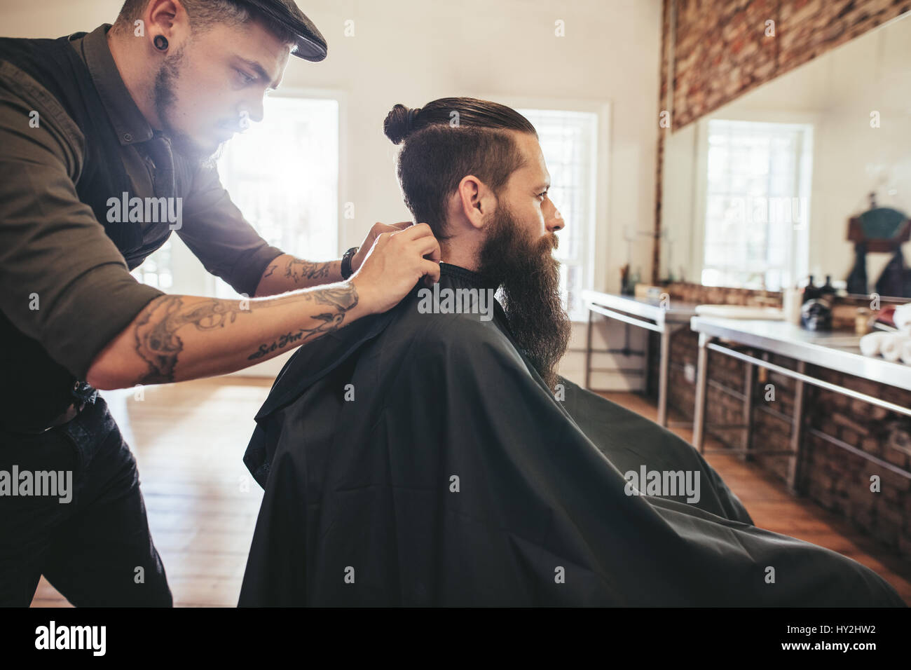 Friseur Client im Barbershop schneiden Haare Cape anziehen. Mann mit Bart sitzt im Friseursalon. Stockfoto