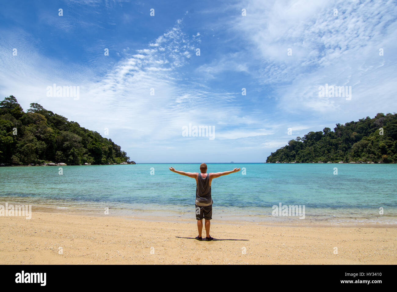 Mann mit Waffen, auf einem leeren idlic paradiesischen Strand in eine leere Bucht mit Bäumen gesäumten Landzunge. Stockfoto