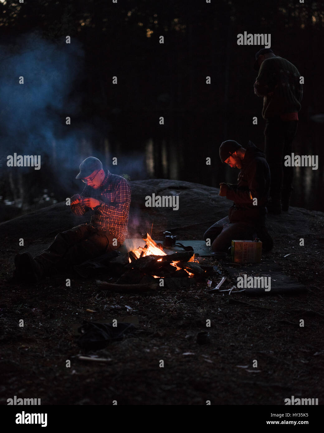 Schweden, Blekinge, Olofstrom, Männer sitzen am Lagerfeuer in der Dämmerung Stockfoto