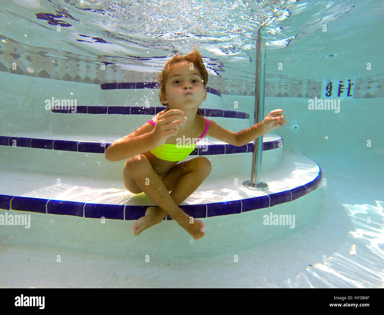 unter Wasser im Pool, kleines Mädchen Posen sitzt auf Schritte, Stockfoto