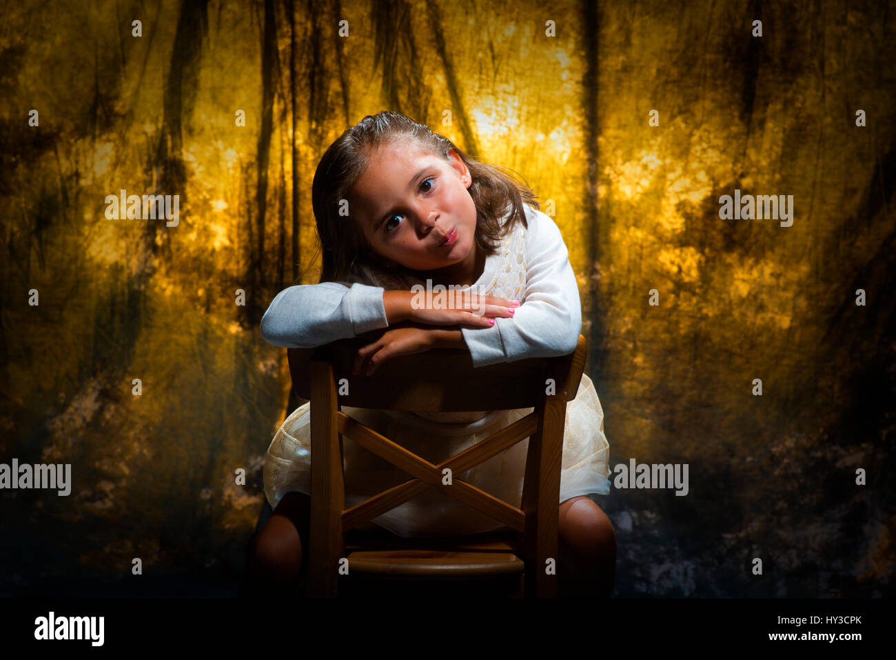 junges Mädchen im Studio posieren Goldgrund sitzen auf Stuhl Stockfoto
