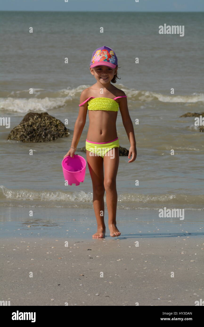 junges Mädchen am Strand gelben Badeanzug und rosa Eimer Stockfoto