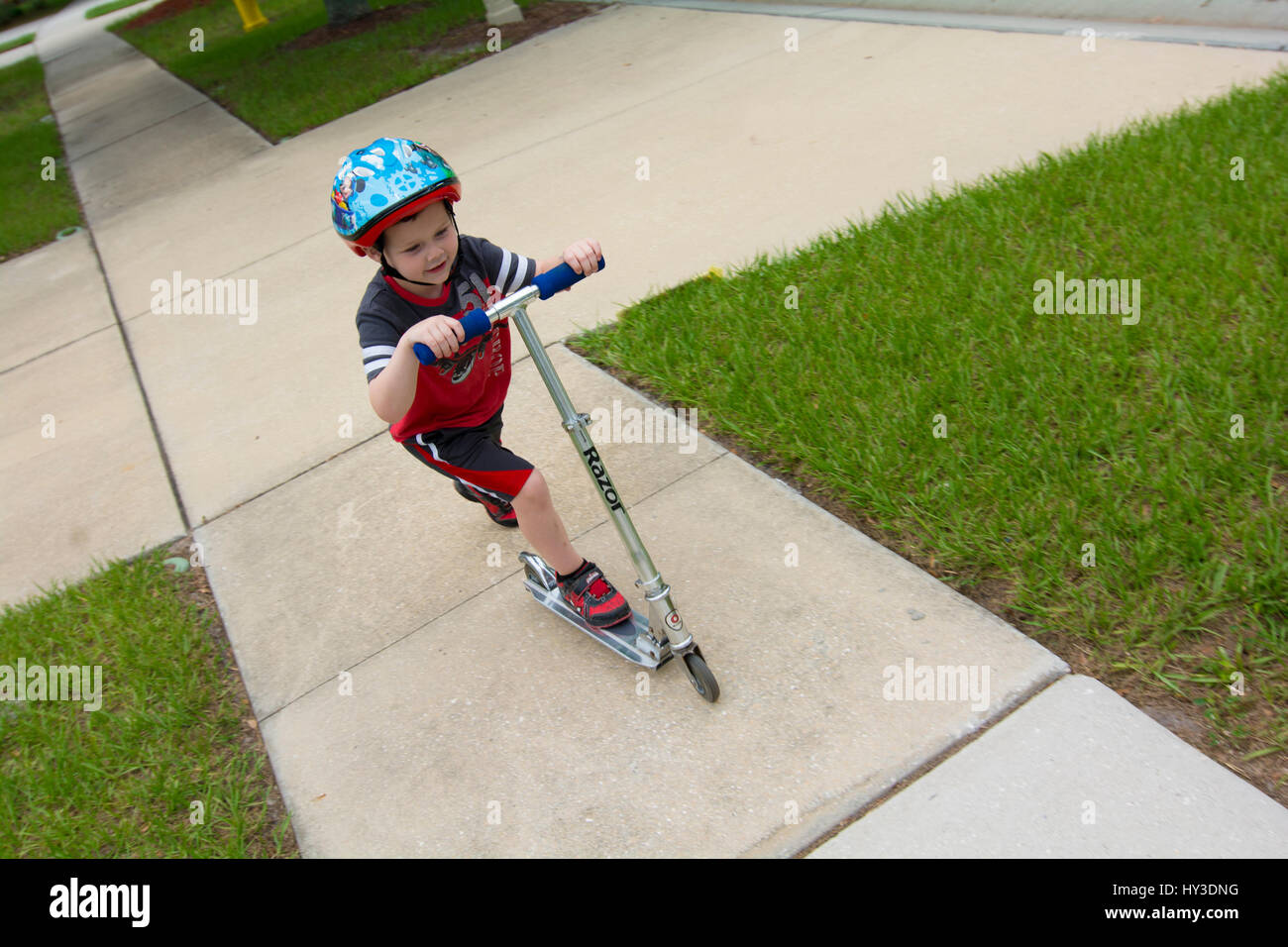 kleiner Junge Reiten Scooter auf Bürgersteig Stockfoto
