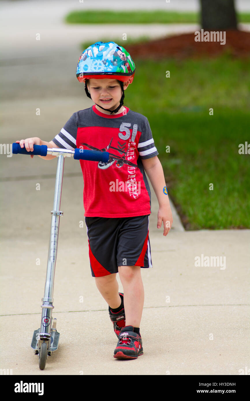 kleiner Junge gehen Scooter auf Bürgersteig Stockfoto