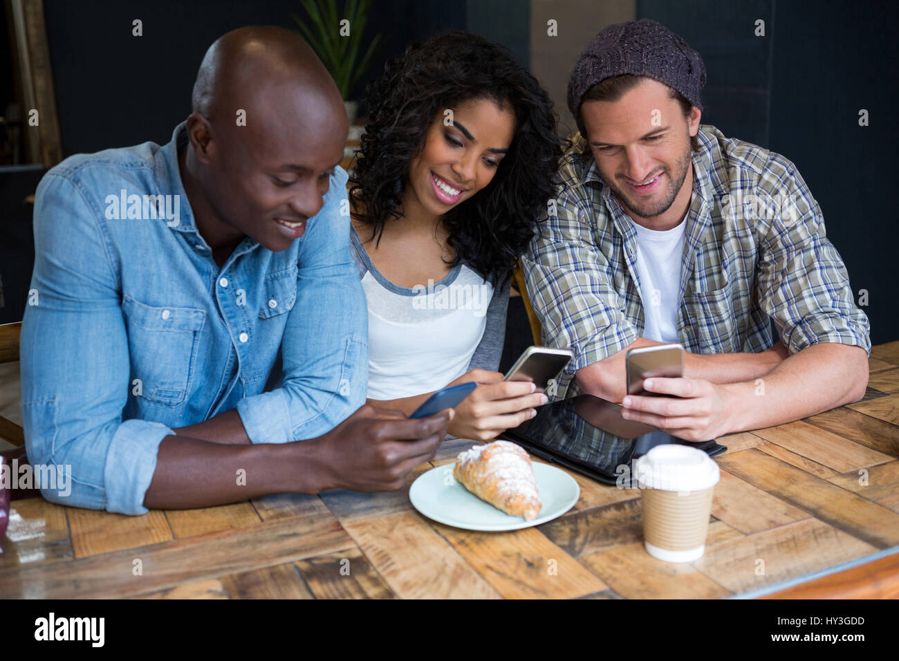 Lächelnde junge Freunde, die mit Smartphones am Tisch im Café Stockfoto