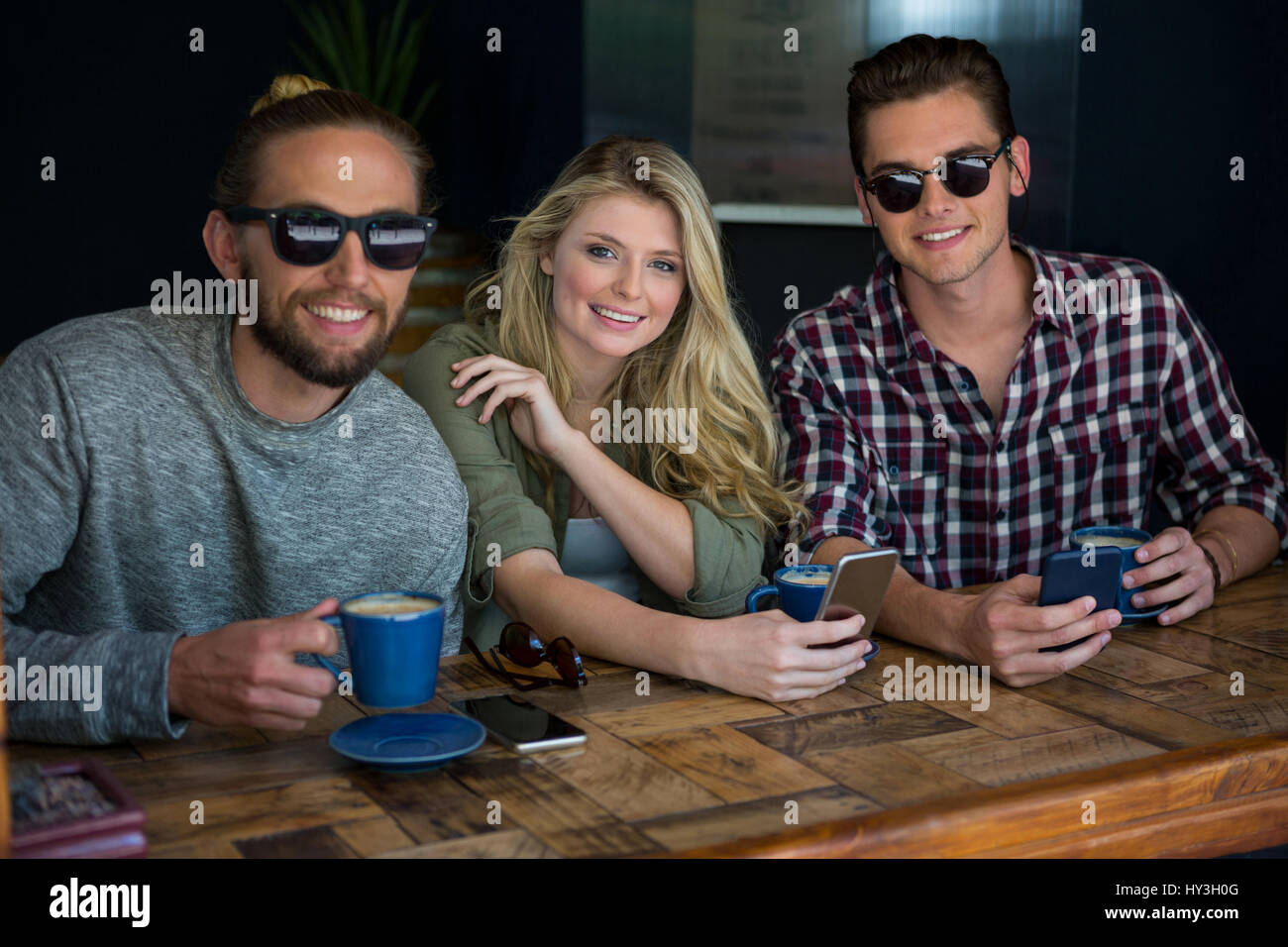Porträt der Frau mit männlichen Freunden das Tragen von Sonnenbrillen in Coffee-shop Stockfoto