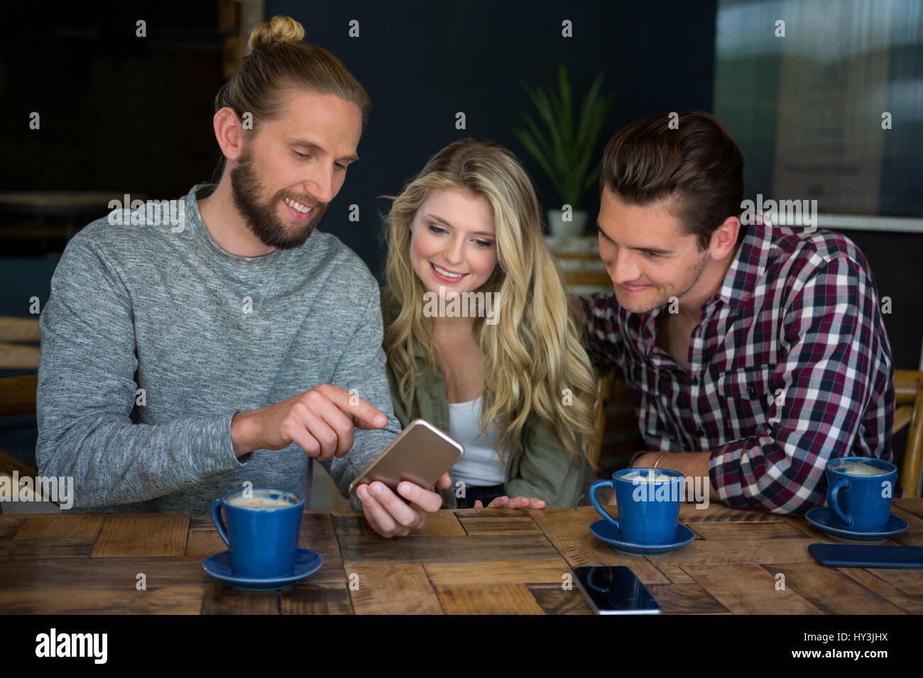 Junger Mann zeigt Smartphone mit Freunden am Tisch im Café Stockfoto