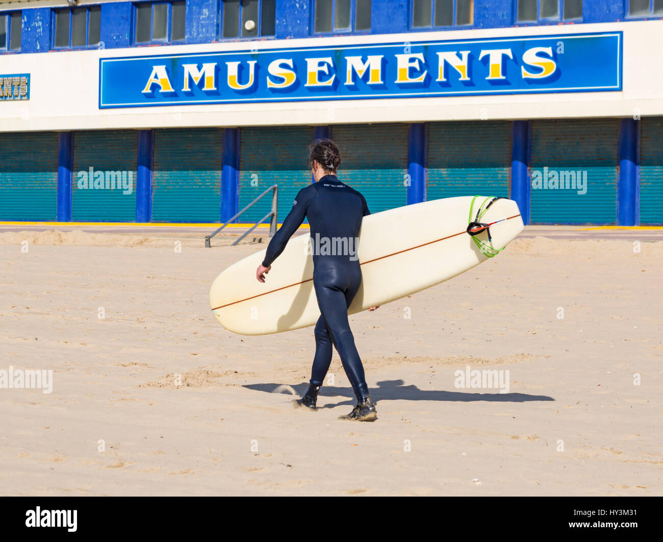 Bournemouth - Surfer mit Surfbrett, vorbei an Vergnügungen Arcade in Bournemouth Beach im März Stockfoto