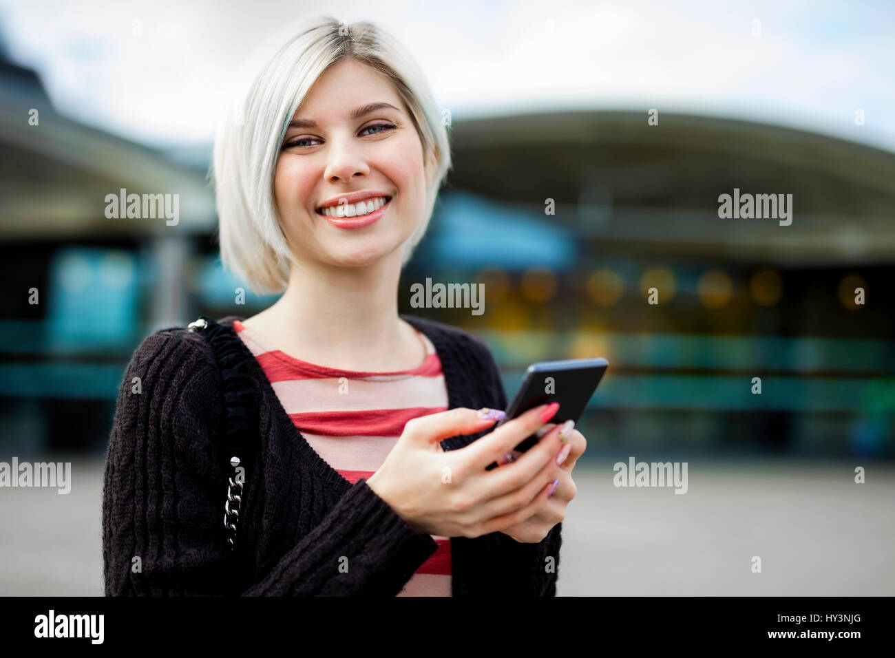 Bei der Verwendung von Handy vor Bahnhof lächelnde Frau Stockfoto