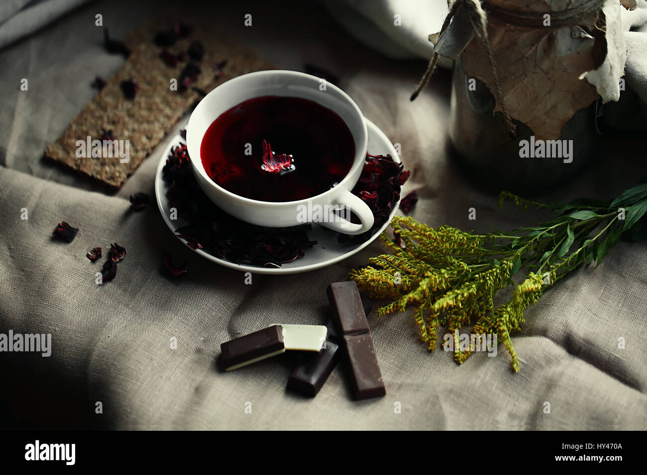 Draufsicht auf weißem Porzellan Glastasse roter Tee Karkade auf Leinwand Tischdecke. Hausgemachten Schokoladenkekse, Zitronensaft, Zimtstangen, Honig und thuj Stockfoto