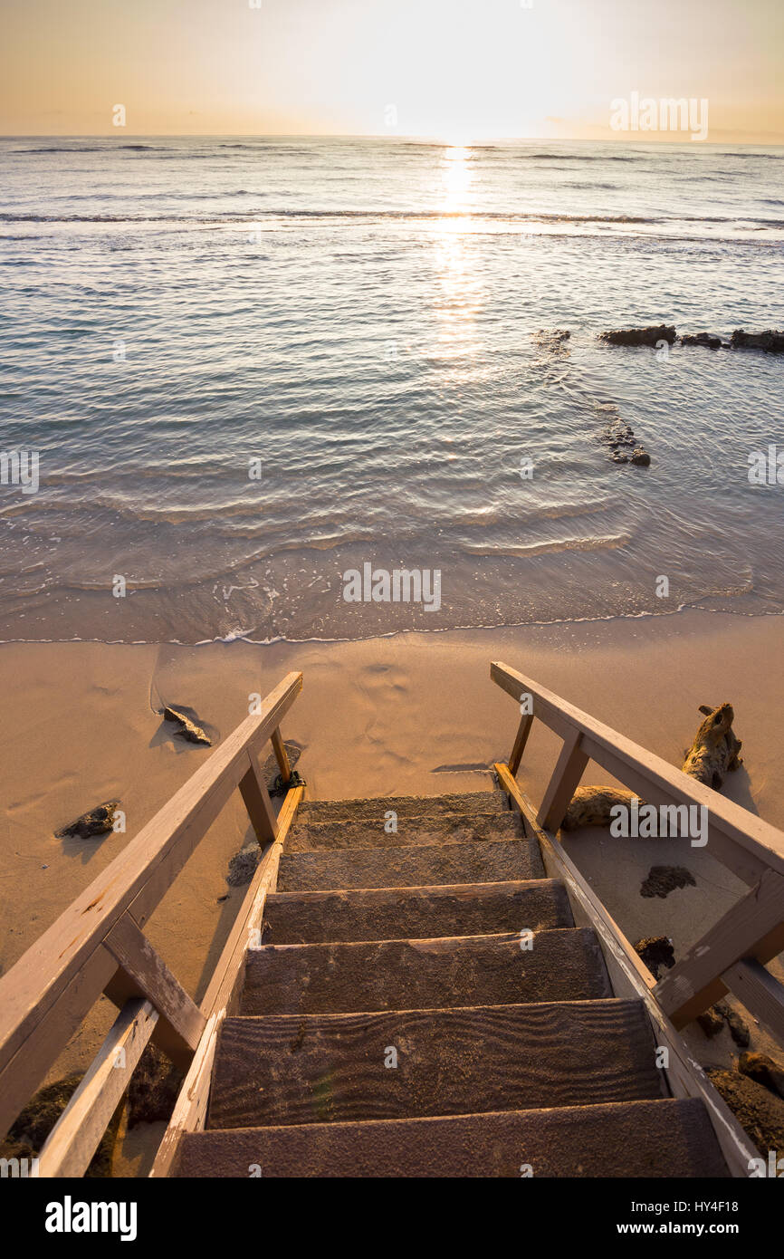 Privater Zugang zu einem öffentlichen Strand auf Oahu Hawaii bei Sonnenuntergang mit der Treppe im Mittelpunkt und das Wasser heraus verwischt. Stockfoto
