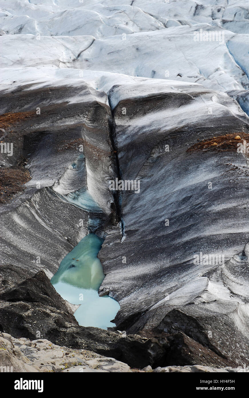 Über Ansicht auf isländischen Gletscher schmelzen und drehen in eine schmutzige schwarze Gletscherspalte des Eises mit einem türkisfarbenen See von Schmelzwasser im Split Stockfoto