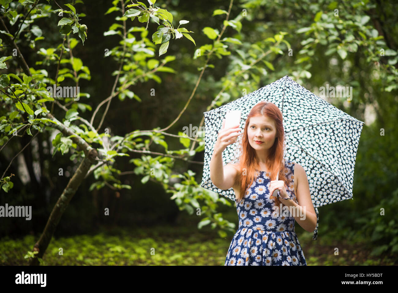 Finnland, Pirkanmaa, Tampere, Frau mit geblümten Kleid mit Regenschirm in Park und unter selfie Stockfoto