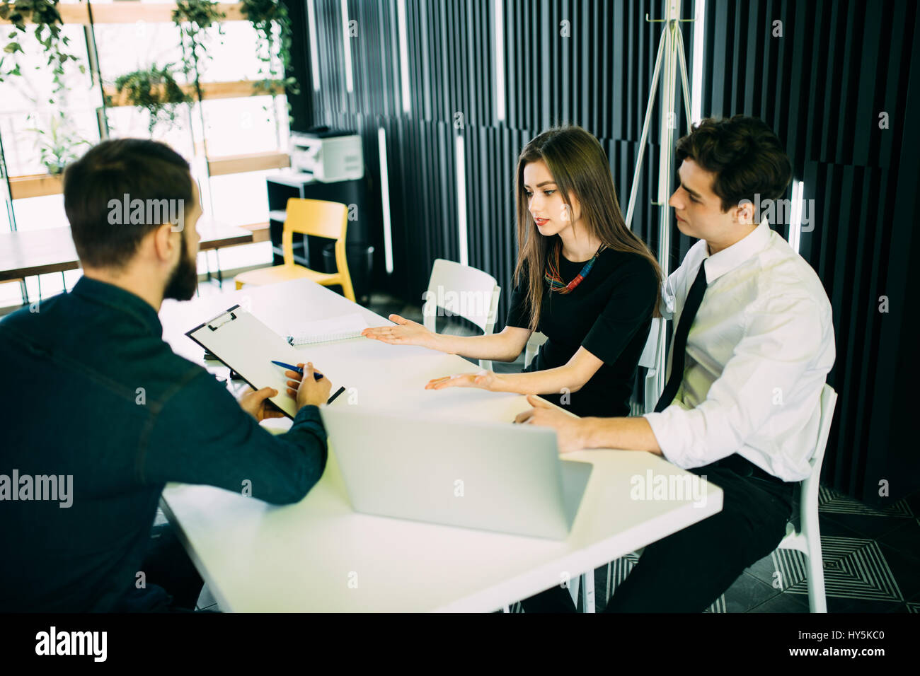 Es scheint ein guter Vorschlag. Fröhliches junges Paar Bindung zueinander und lächelnd beim betrachten einige Mann sitzt vor ihnen und gest. Stockfoto