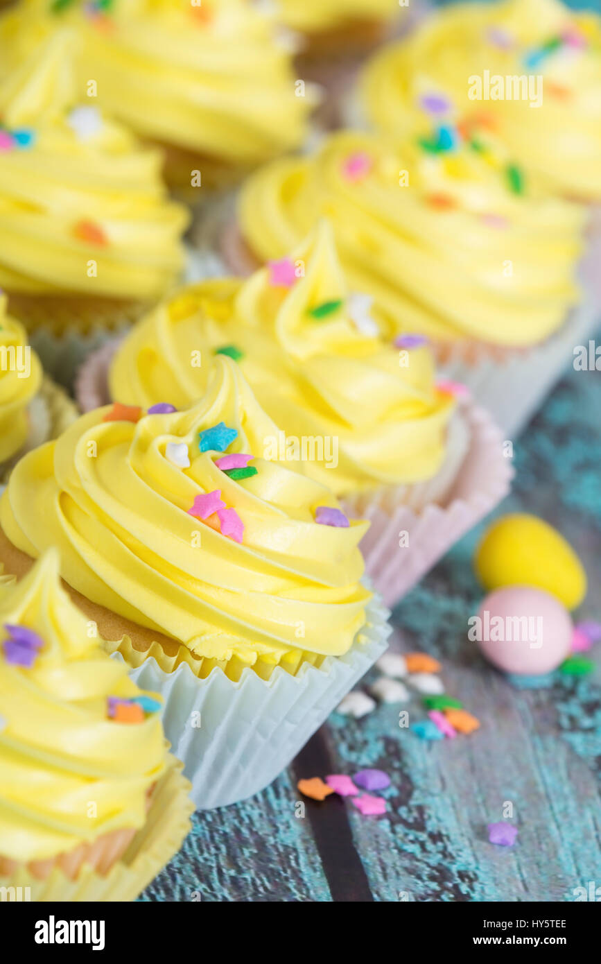 Reihe von gelben Oster-Cupcakes mit Süßigkeiten und Streusel auf Vintage Holztisch Stockfoto