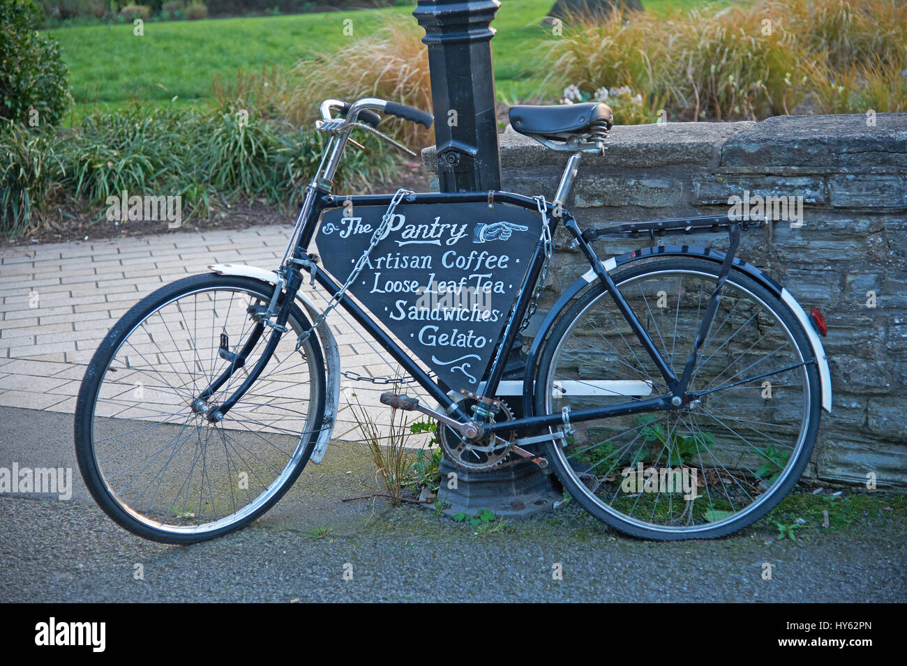 Ein altes schwarzes Fahrrad an einen Laternenpfahl gekettet und lehnte sich gegen eine Steinmauer. Stockfoto