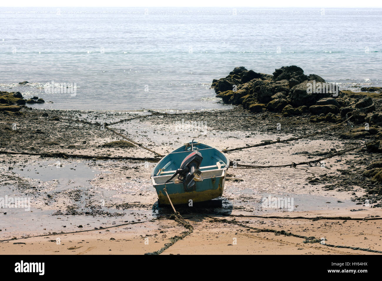 Ein kleines Boot mit Außenbordmotor schwer gesichert, großen Felsen am Strand bei Ebbe zu einem schwindenden Horizont schauen. Stockfoto
