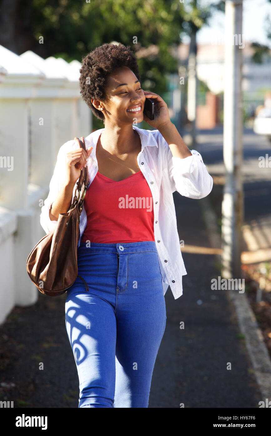 Porträt der glückliche junge Afrikanerin Straße entlang und telefonieren mit Handy Stockfoto