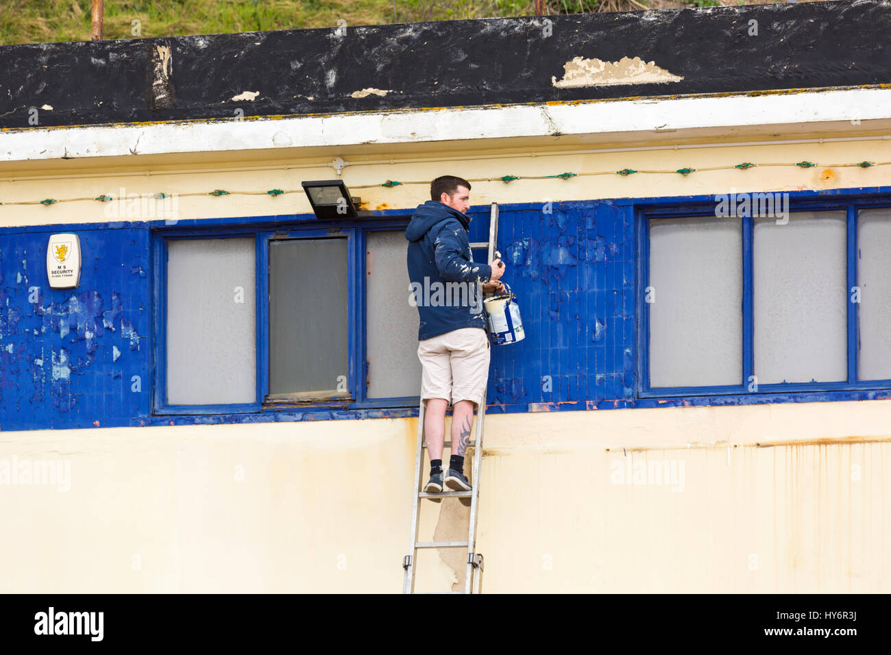 Mann auf Leiter mit Topf Farbe malen Vergnügungen Arcade aufbauend auf Bournemouth Promenade im April Stockfoto