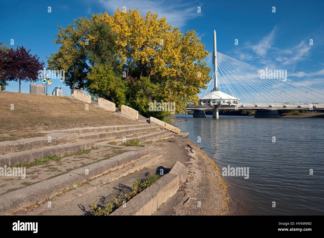 Ufer entlang des Roten Flusses an The Forks (im Hintergrund die Esplanade Riel Fußgängerbrücke), Winnipeg, Manitoba, Kanada Stockfoto