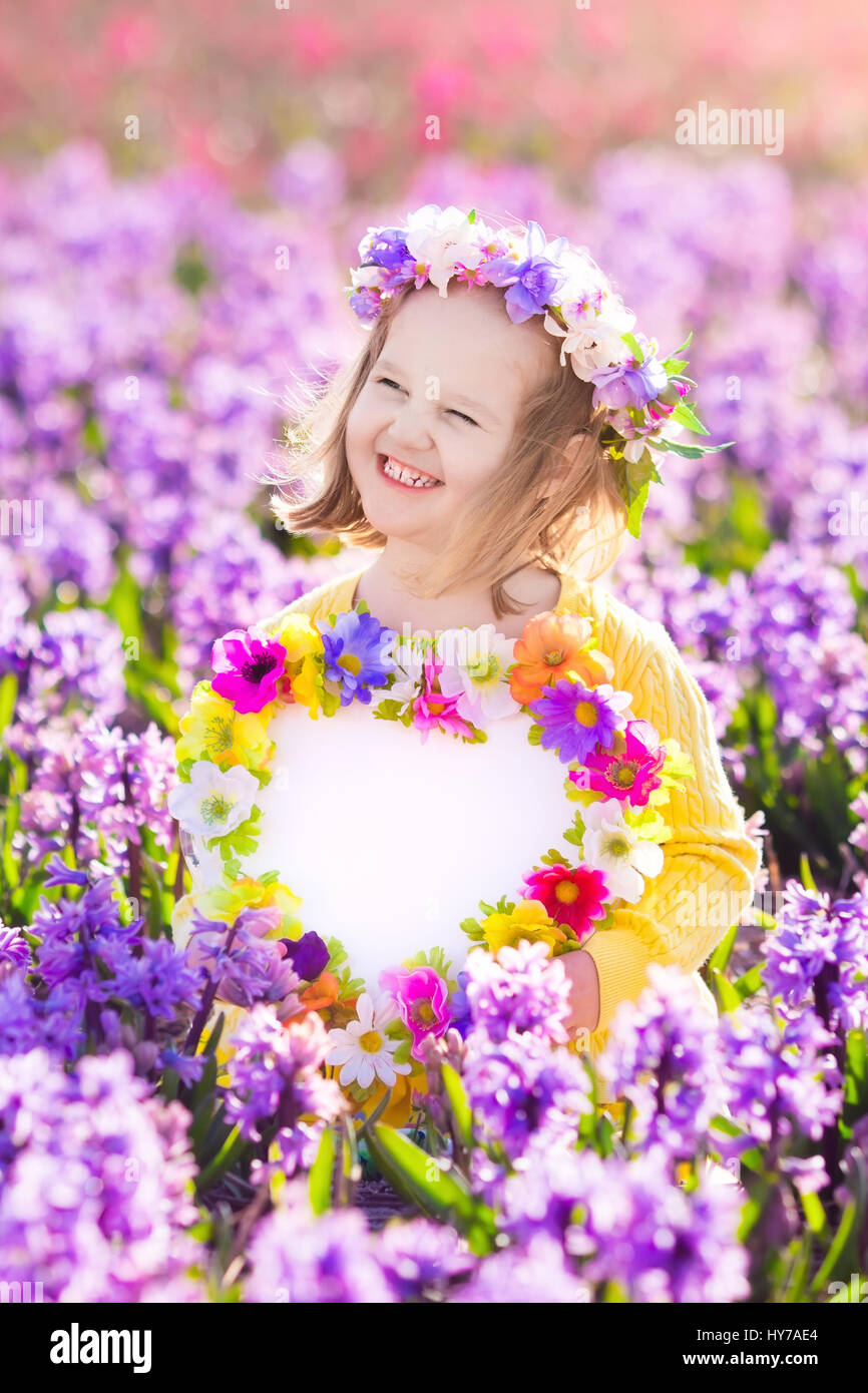 Kind spielt auf Hyazinthe Gebiet. Kleines Mädchen hält ein Herz aus Holz Form Kreide Board steht in einem Park mit Hyazinthen Frühlingsblumen. Textfreiraum für Stockfoto