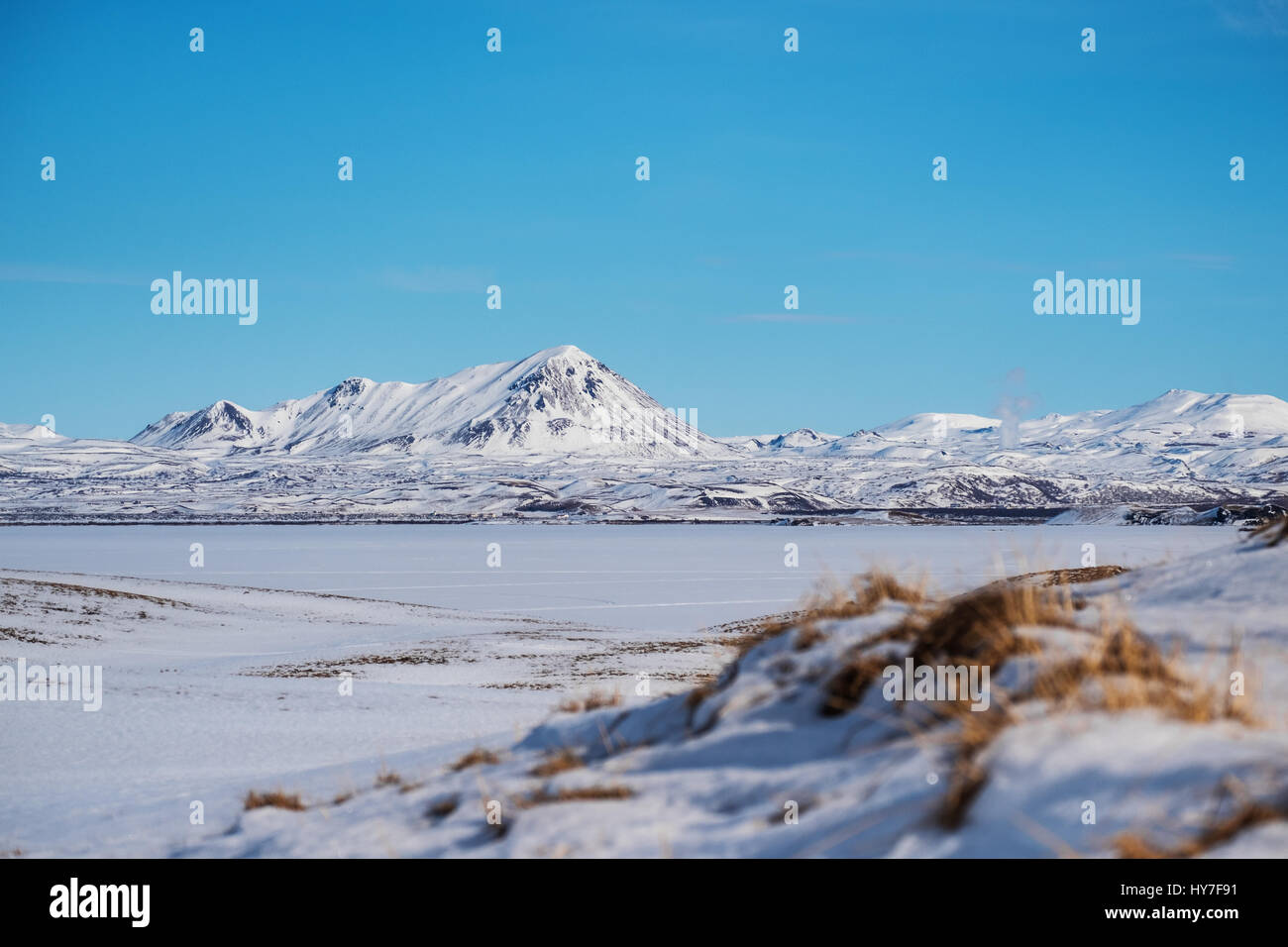 Säen Sie Winterlandschaft, Feld mit gefrorenen See und Schnee Berg mit klaren blauen Himmel Stockfoto