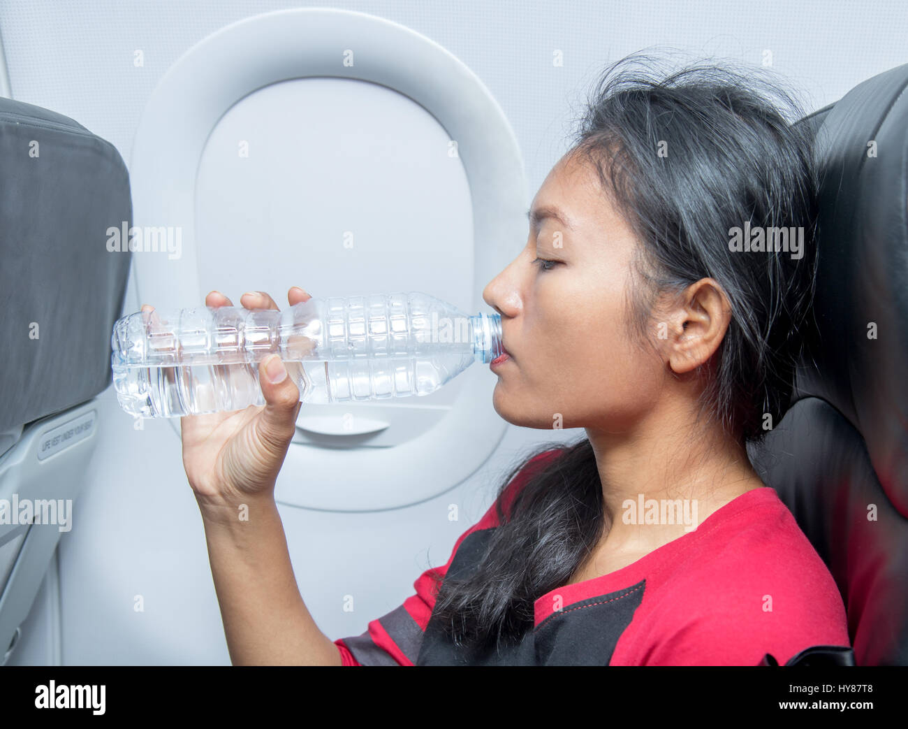 Frau im Flugzeug trinkt Wasser aus einer Plastikflasche. Ein Passagierflugzeug fliegen in das Getränk erfrischt aus seiner Flasche. Stockfoto