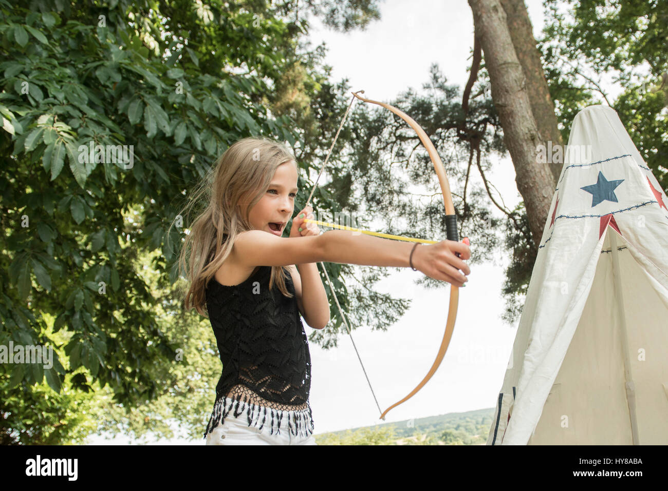 Ein junges Mädchen schießt einen Pfeil und Bogen, während draußen spielen Stockfoto