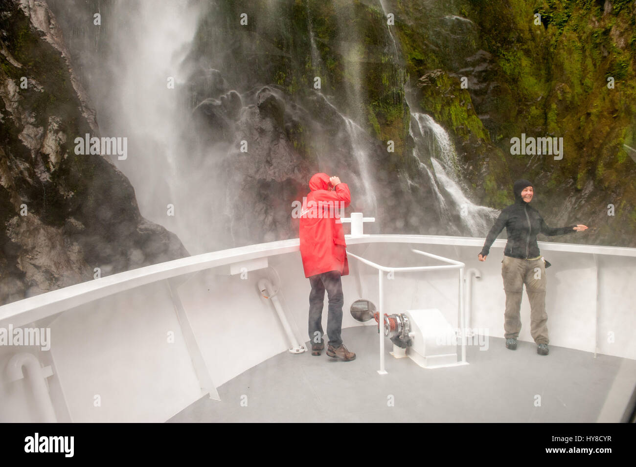 Touristen, die in der Nähe eines Wasserfalls im Milford Sound, Mammutt Nationalpark, Neuseeland Kreuzfahrt Stockfoto